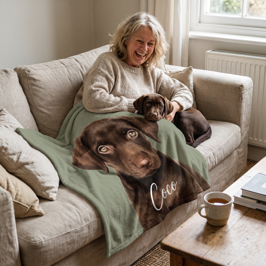 Woman laughing on the sofa under a personalised watercolour labrador blanket with her puppy